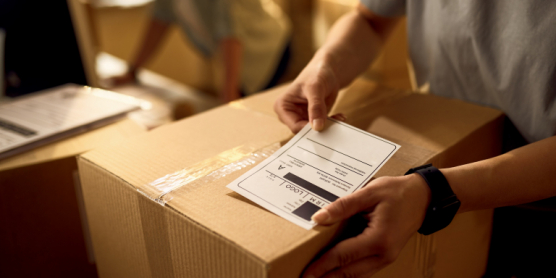 Nahaufnahme einer Person, die ein Retourenlabel auf ein Paket klebt – Symbol für schnellen Retourenservice.