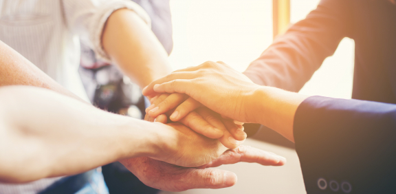 Mehrere Hände übereinander gestapelt, symbolisieren Zusammenhalt und Unterstützung.