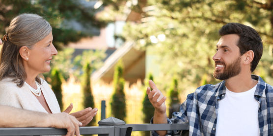 Zwei Paare unterschiedlichen Alters unterhalten sich freundlich im Freien. Nachbarschaft kennenlernen nach dem Umzug.