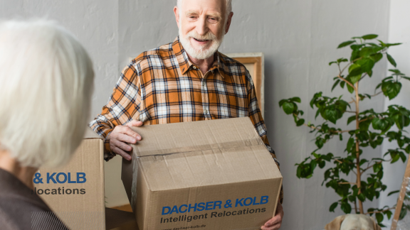 Senior trägt Umzugskarton mit DACHSER & KOLB – sicherer Seniorenumzug in gehobene Wohnresidenzen