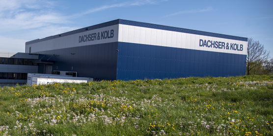 Modernes Gebäude des Umzugsunternehmens DACHSER & KOLB mit Lagerhalle und Bürotrakt, umgeben von grüner Wiese.