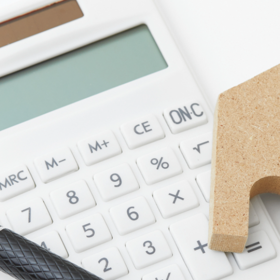 Taschenrechner, Stift und Holzhaus – Symbole für finanzielle Planung und Tipps zur Berechnung von Umzugskosten.