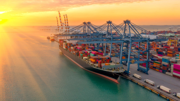 Beladenes Containerschiff einer Reederei am Kai im großen Hafen mit Kranen bei Sonnenuntergang.