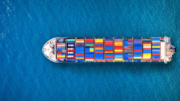 Luftaufnahme eines großen Containerschiffs beladen mit bunten Frachtcontainern auf offener See.