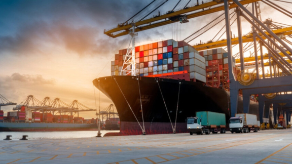 Containerschiff wird im Hafen bei Sonnenuntergang von Kränen und Lkw be- und entladen