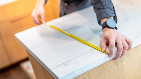 Hand misst eine Küchenarbeitsplatte mit einem Maßband, um präzise Maße für die Küchenmontage zu nehmen.