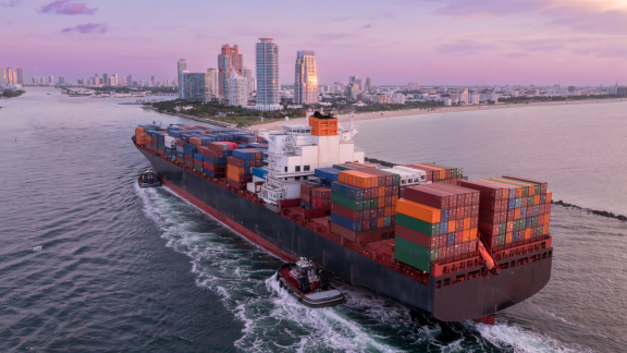 Containerschiff mit Schleppern fährt in einen Stadthafen ein – Experten für reibungslose Seefracht-Umzüge weltweit.