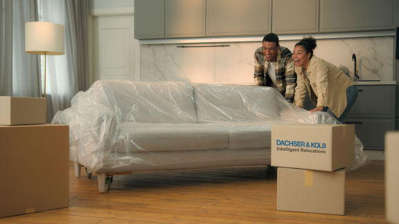 Paar verpackt Sofa mit Schutzfolie, Emballage für Umzug in Wohnung, Umzugskartons im Raum.