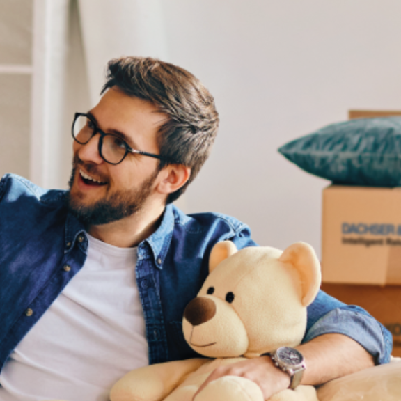 Vater und Tochter lachen beim Umzug, umgeben von DACHSER & KOLB Kartons – Qualität durch FIDI-Zertifizierung.
