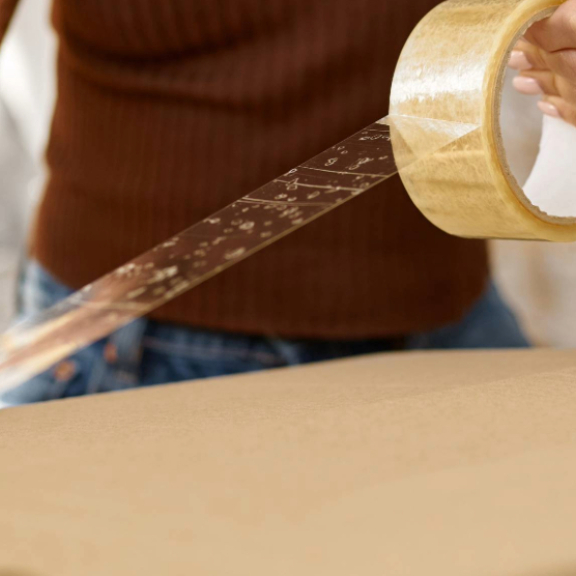 Nahaufnahme einer Person, die einen Umzugskarton mit Klebeband verschließt, typisch für einen 