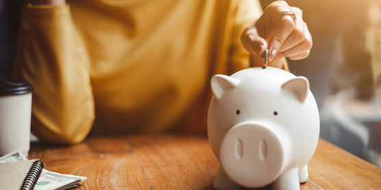 Hand steckt Münze in Sparschwein. Symbolisiert Sparen und flexible Finanzierung für Umzug auf Ratenzahlung.