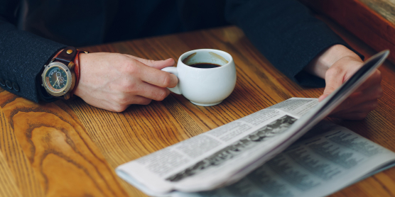 Person liest Zeitung und trinkt Kaffee – Moment der Information und Reflexion über das aktuelle Tagesgeschehen.