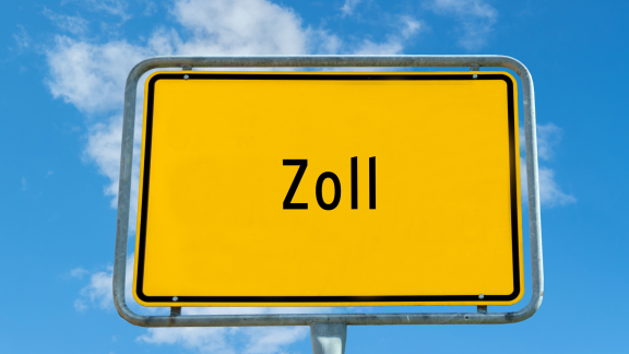 Gelbes Straßenschild mit Aufschrift „Zoll“ vor blauem Himmel als Symbol für Zollkontrolle an der Grenze