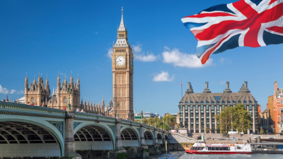 Big Ben und Westminster Bridge in London mit britischer Flagge am blauen Himmel
