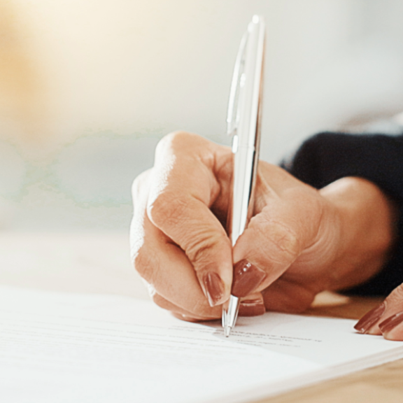 Nahaufnahme einer Hand, die eine Wertgutliste unterschreibt; Fokus auf Stift und Dokument.