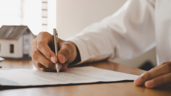 Hand unterschreibt Mietvertrag auf dem Tisch